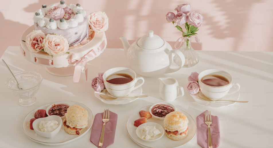 Afternoon tea setup with scones, cream, cake, and roses on a pink themed table setting.