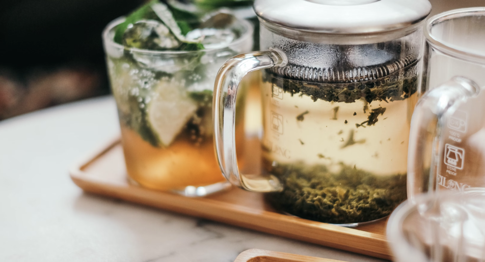 Glass teapot and iced tea with fresh mint and lime on a wooden tray, placed on a marble surface